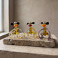Three Lanky Ape lampworked glass monkey figurines in amber glass with different lip colors seated on a travertine slab, handcrafted by Glass by Iness in L'viv Ukraine