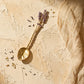 Single lavender cast pewter serving spoon with purple enamel on textured stone surface with dried lavender buds and linen
