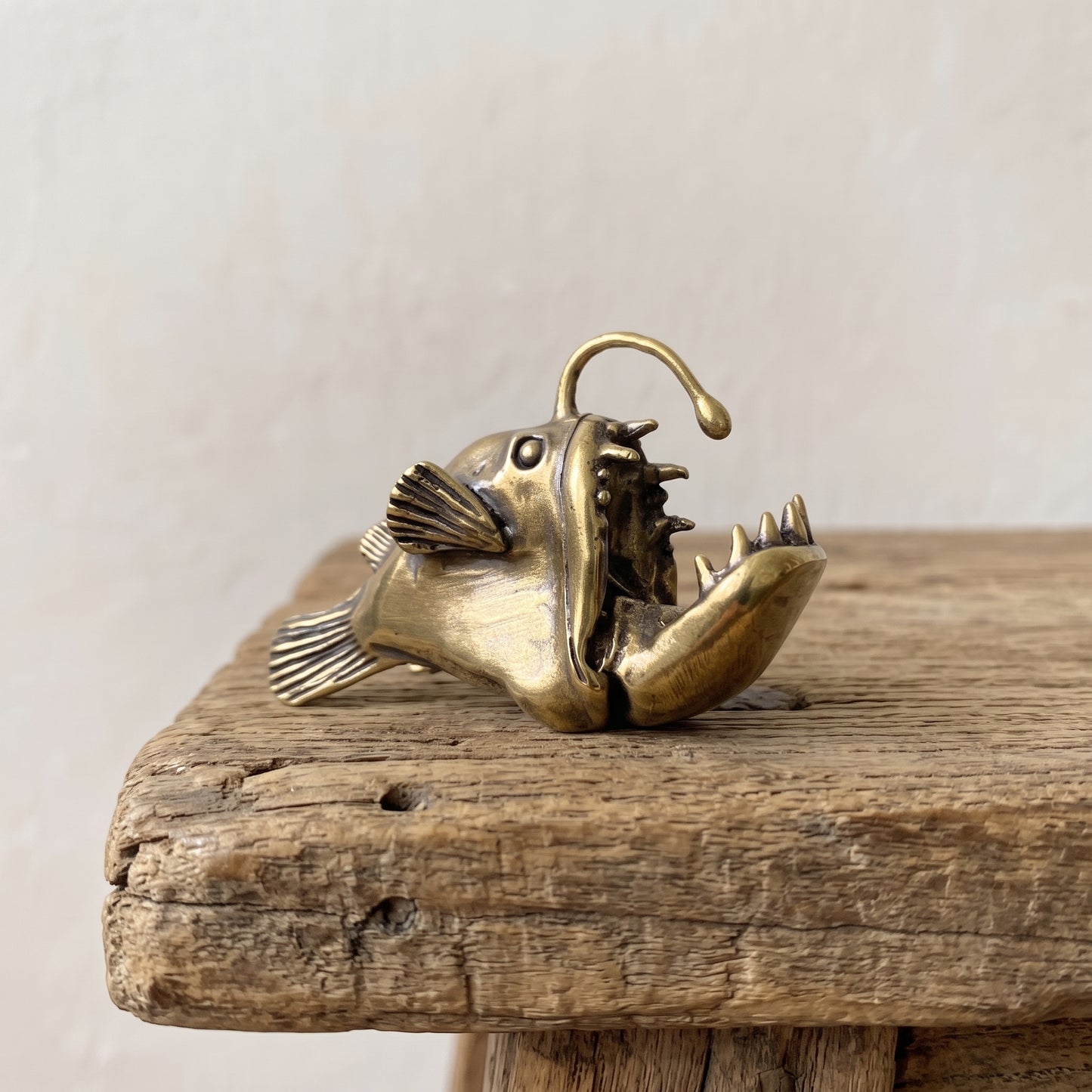 Brass anglerfish figurine with open jaw, needle teeth, and arcing lure, antique patina finish