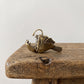 Side view of a brass anglerfish figurine showing its gaping jaw, flared fins, and overhead lure
