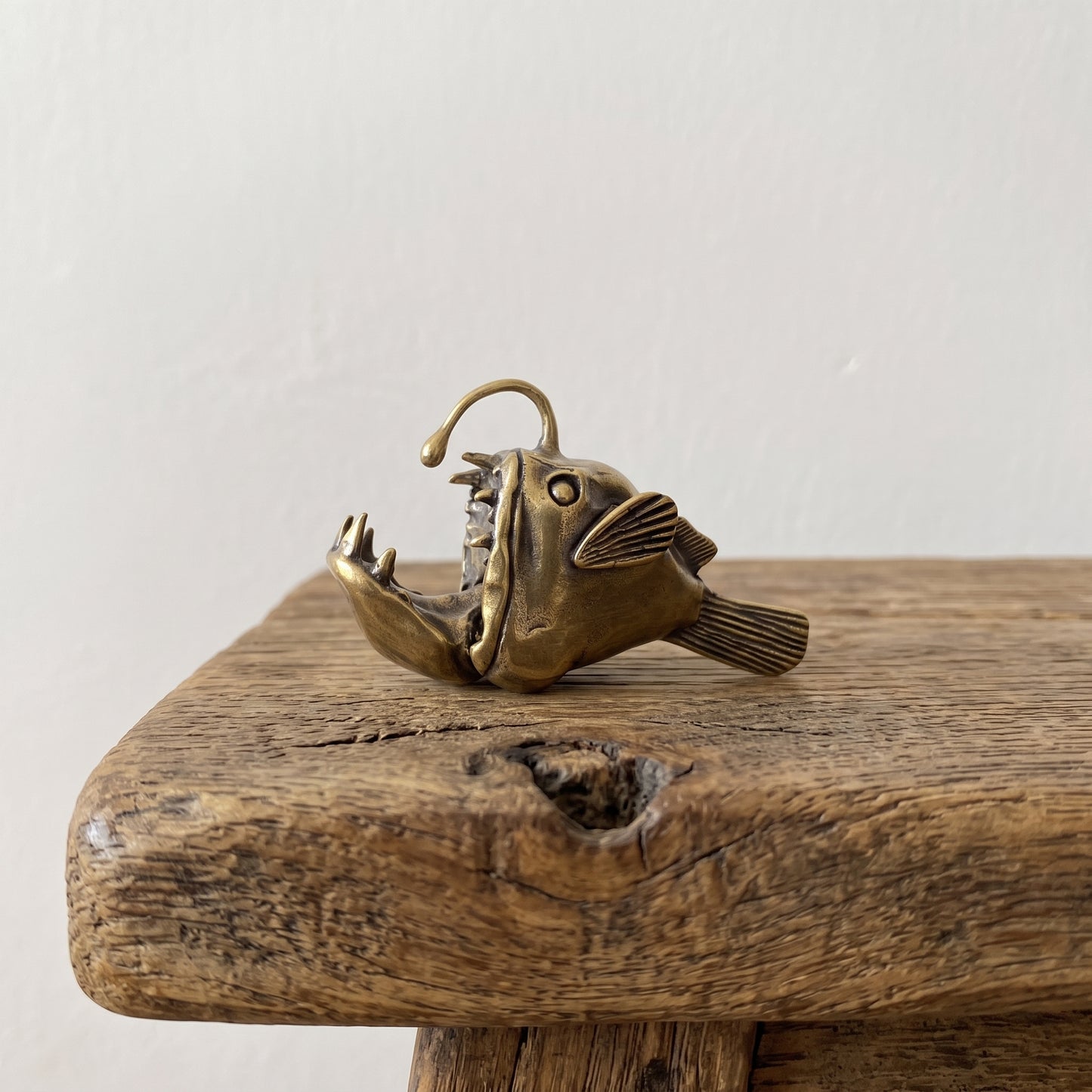 Side view of a brass anglerfish figurine showing its gaping jaw, flared fins, and overhead lure