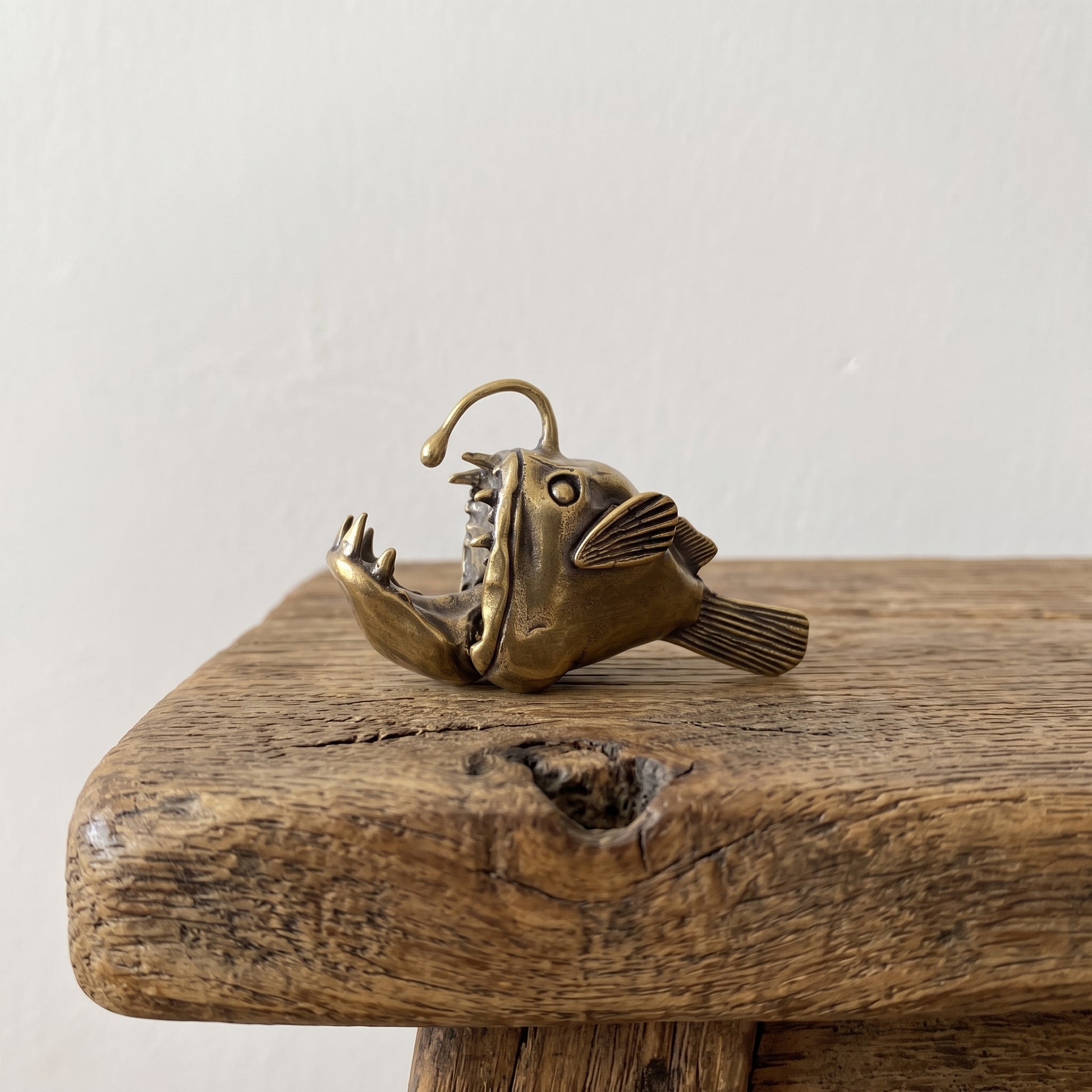 Side view of a brass anglerfish figurine showing its gaping jaw, flared fins, and overhead lure