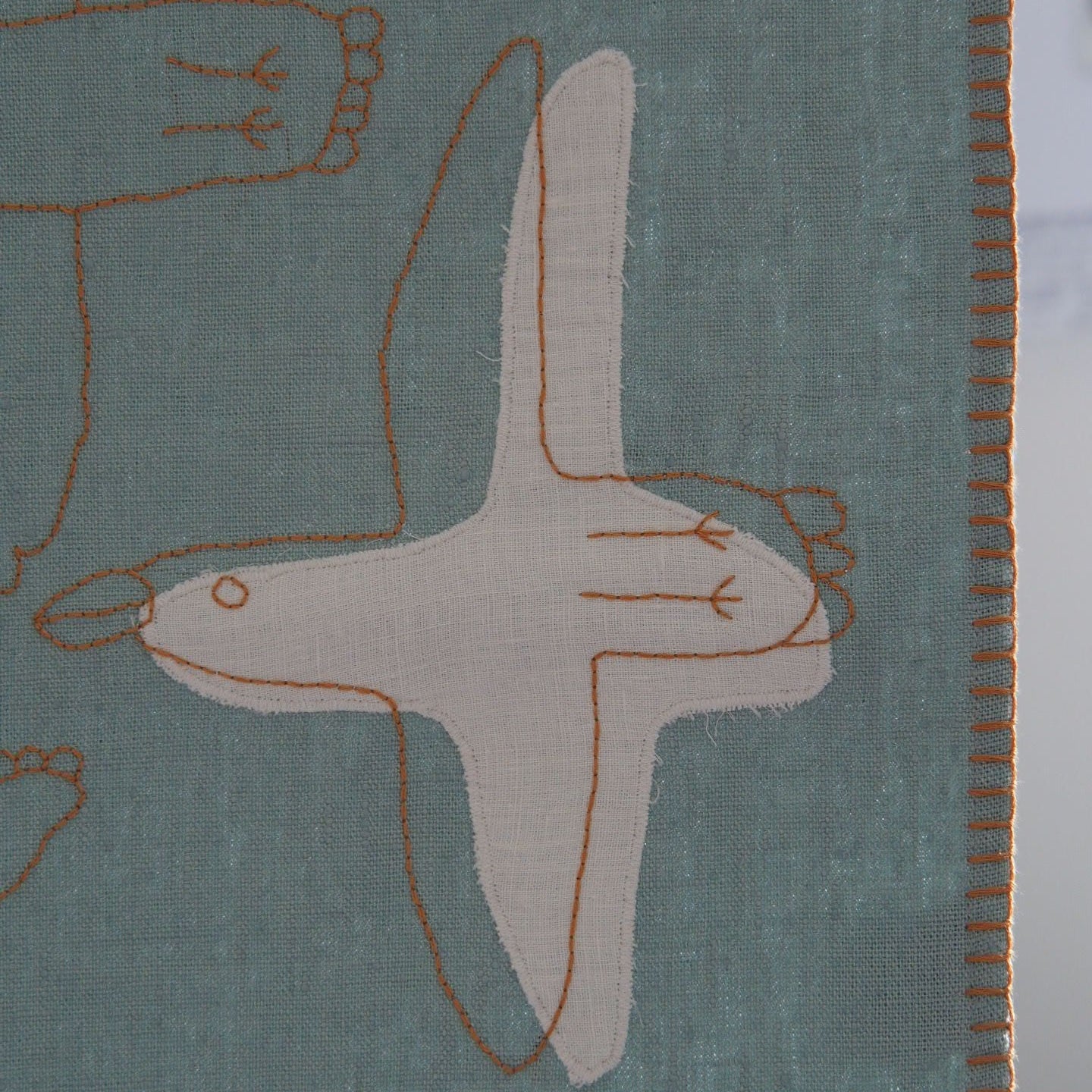 Detail of organic linen baby blanket showing hand-rendered figure and stitched edge, naturally dyed by Ewelina Lapeyre France