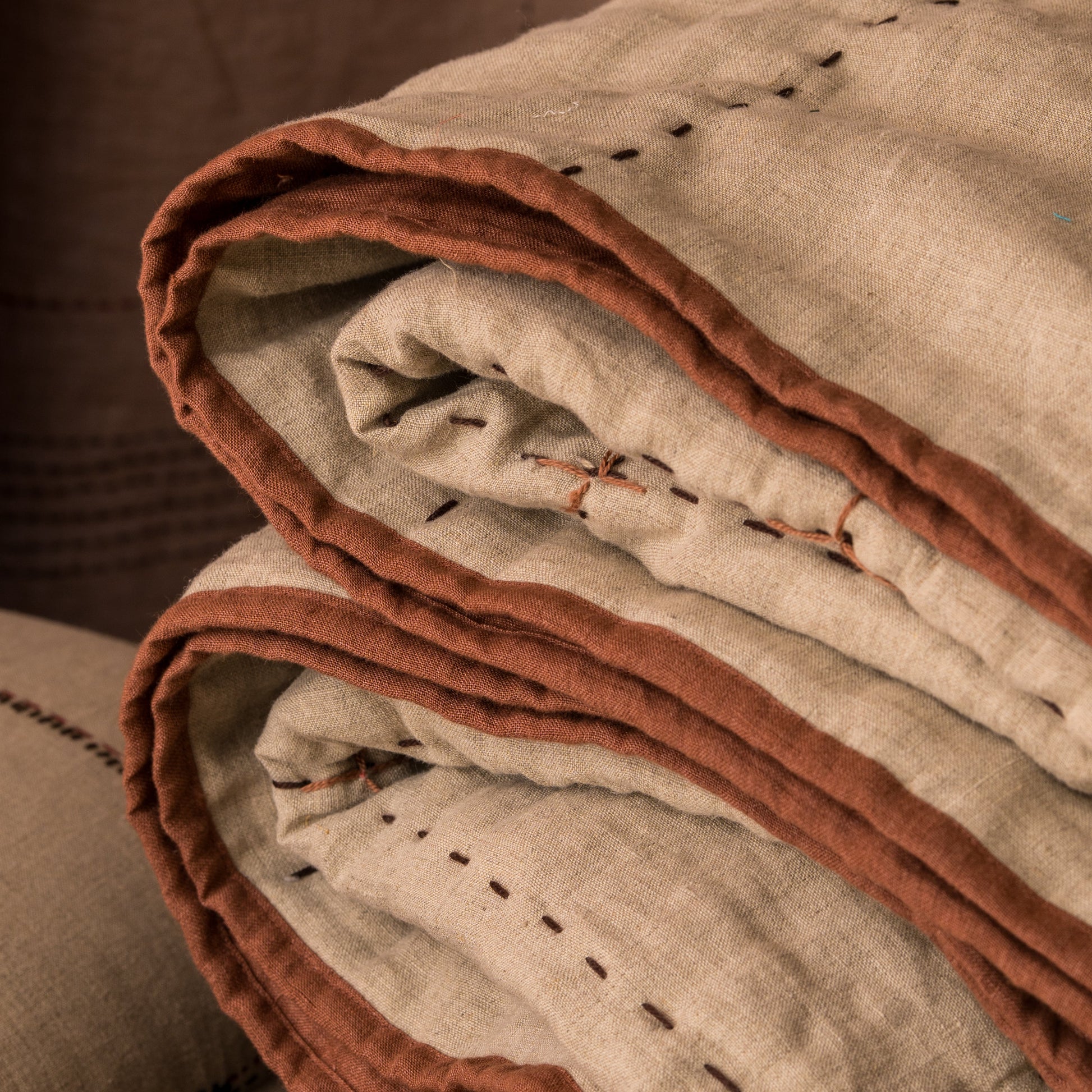 Folded hand-stitched linen quilt in oatmeal with cinnamon terracotta binding, showing layers and hand-stitched dash detail