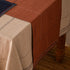 Hand-stitched European linen table runner in eucalyptus terracotta draped over a dining table with a natural linen tablecloth, showing contrast stitch detail
