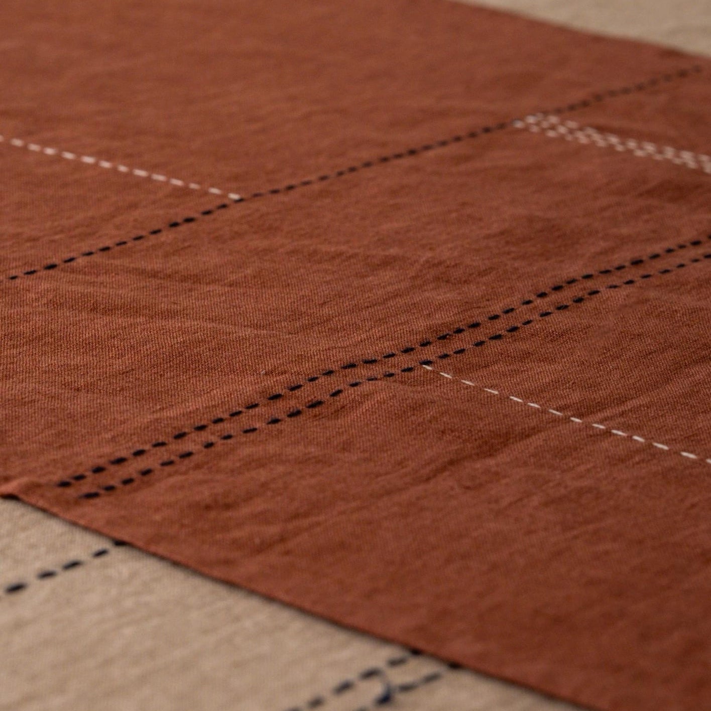 Hand-stitched linen table runner in eucalyptus terracotta draped over a wooden table, showing the full length and hem stitch detail