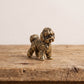Front view of a brass bichon frise figurine showing its bearded muzzle, soft ears and curled fleece in antique patina