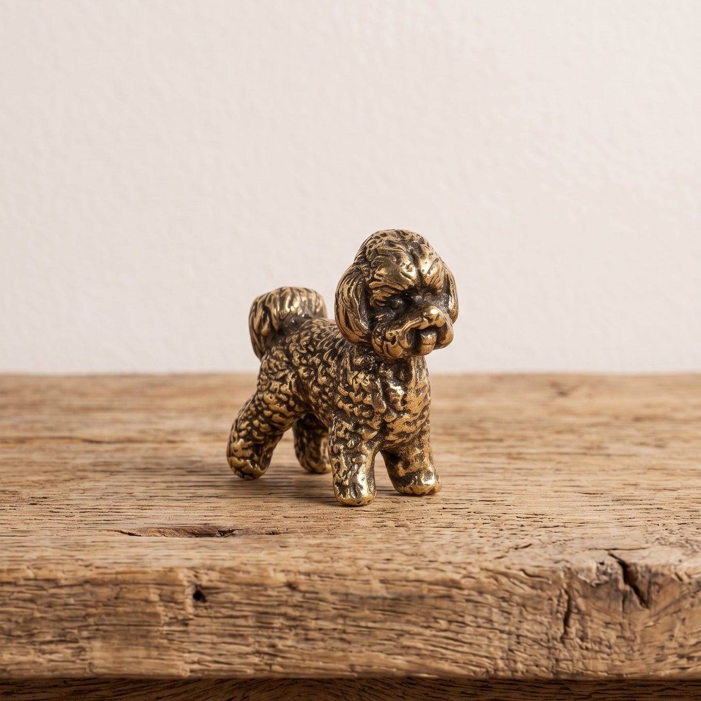 Front view of a brass bichon frise figurine showing its bearded muzzle, soft ears and curled fleece in antique patina