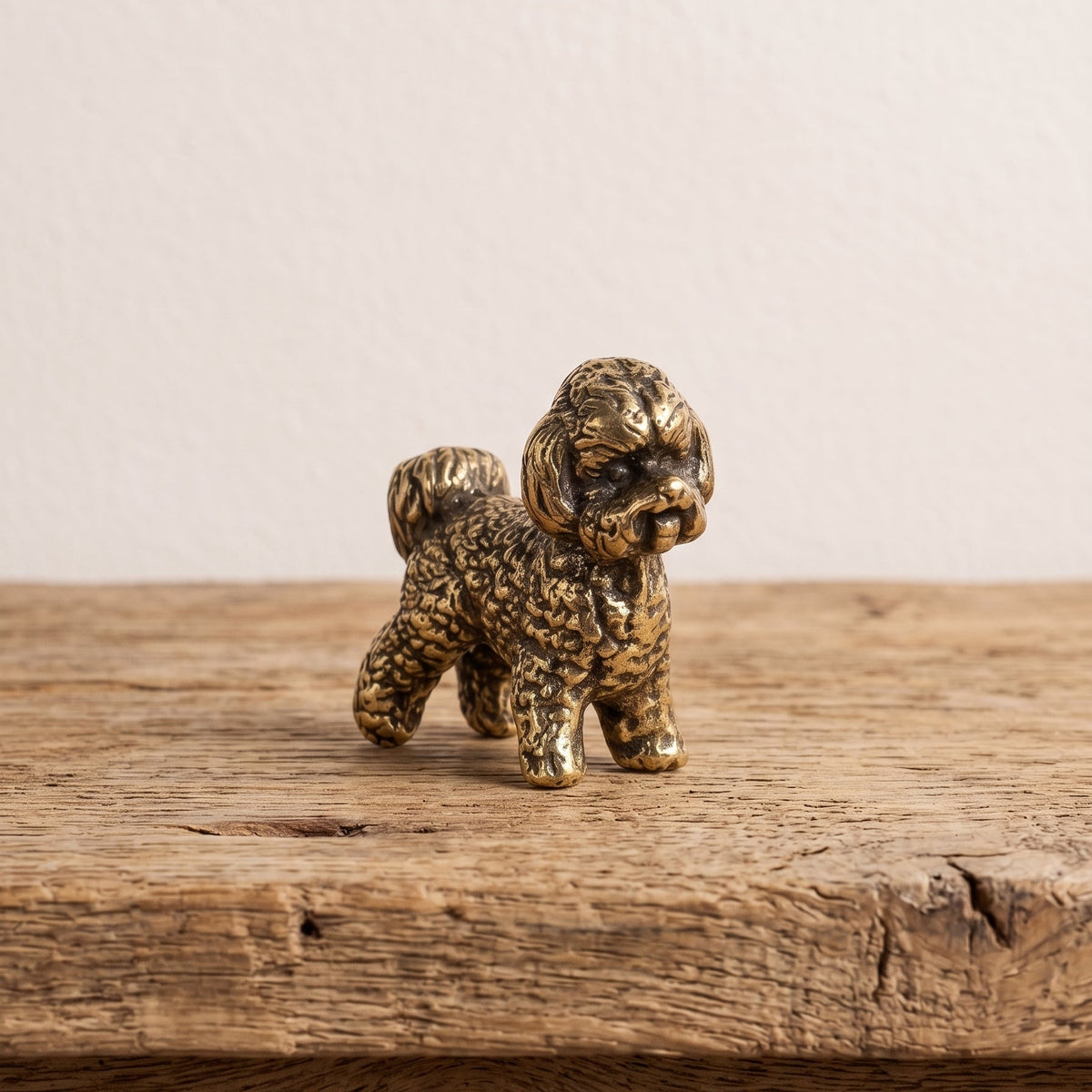 Front view of a brass bichon frise figurine showing its bearded muzzle, soft ears and curled fleece in antique patina