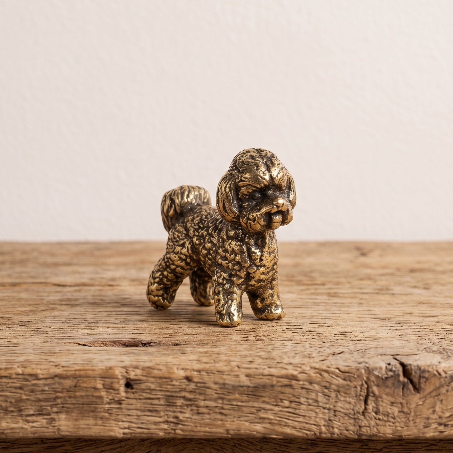 Front view of a brass bichon frise figurine showing its bearded muzzle, soft ears and curled fleece in antique patina