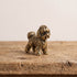 Front view of a brass bichon frise figurine showing its bearded muzzle, soft ears and curled fleece in antique patina