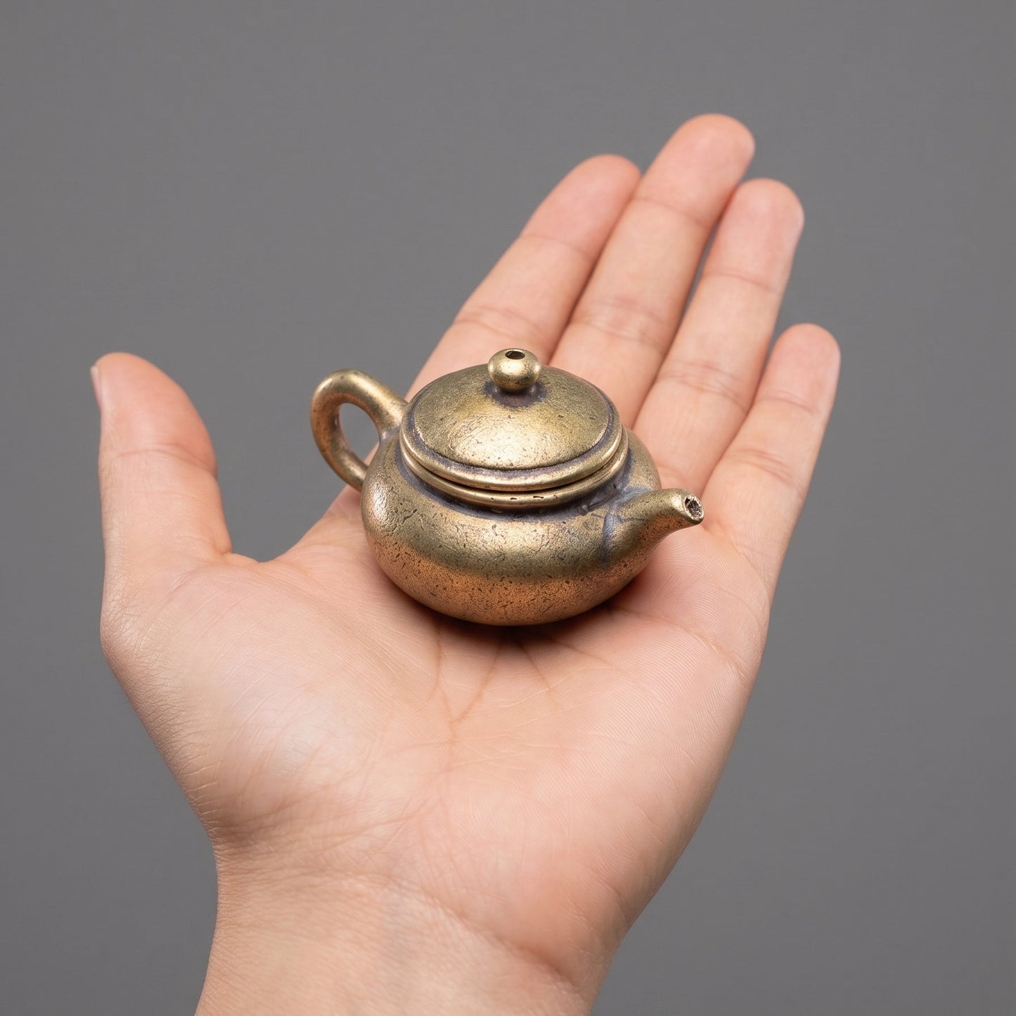 The Little Pot brass teapot held in a hand to show its small size, about 2 inches across