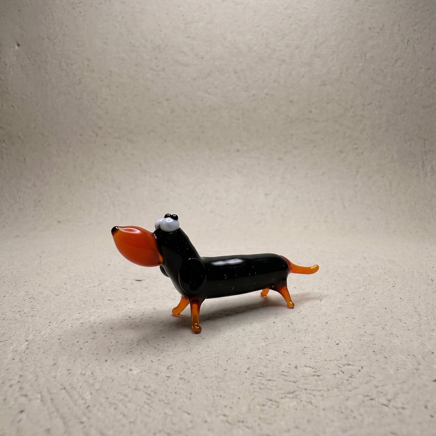 Side profile of The Little Sausage lampworked glass dachshund showing glossy black body with orange legs, ears, and tail
