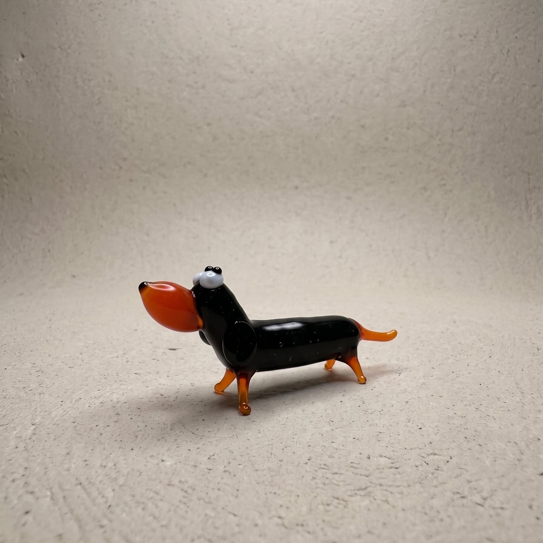 Side profile of The Little Sausage lampworked glass dachshund showing glossy black body with orange legs, ears, and tail
