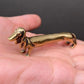 The Long Fellow brass dachshund held in a hand to show its small size, about 3 inches long