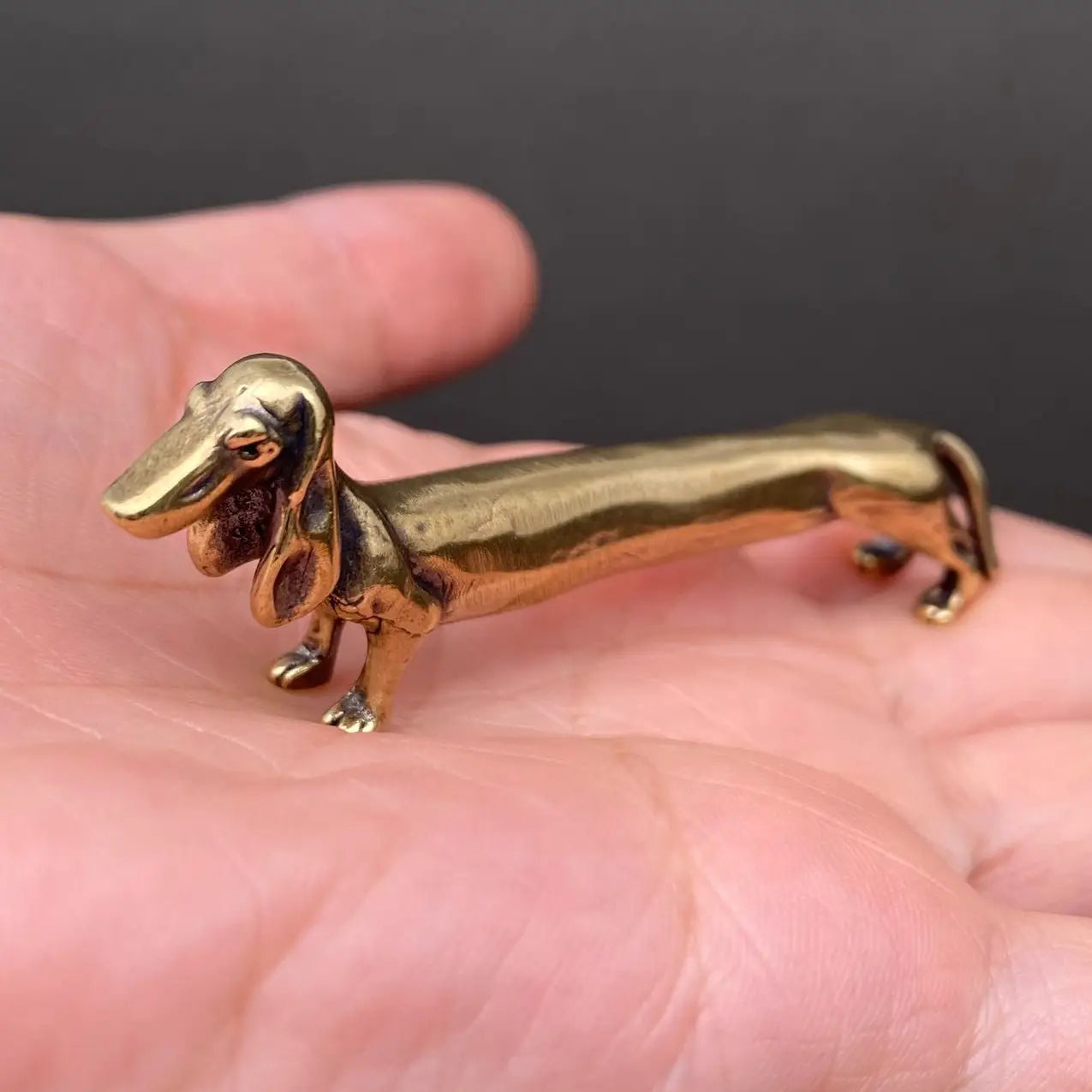 The Long Fellow brass dachshund held in a hand to show its small size, about 3 inches long