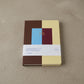 Two-year monthly journal with a color-block cover in chocolate brown, butter yellow, sky blue and burgundy, gold-foil lettering reading Monthly Journal 2027 / 2028, shown with its paper belly band
