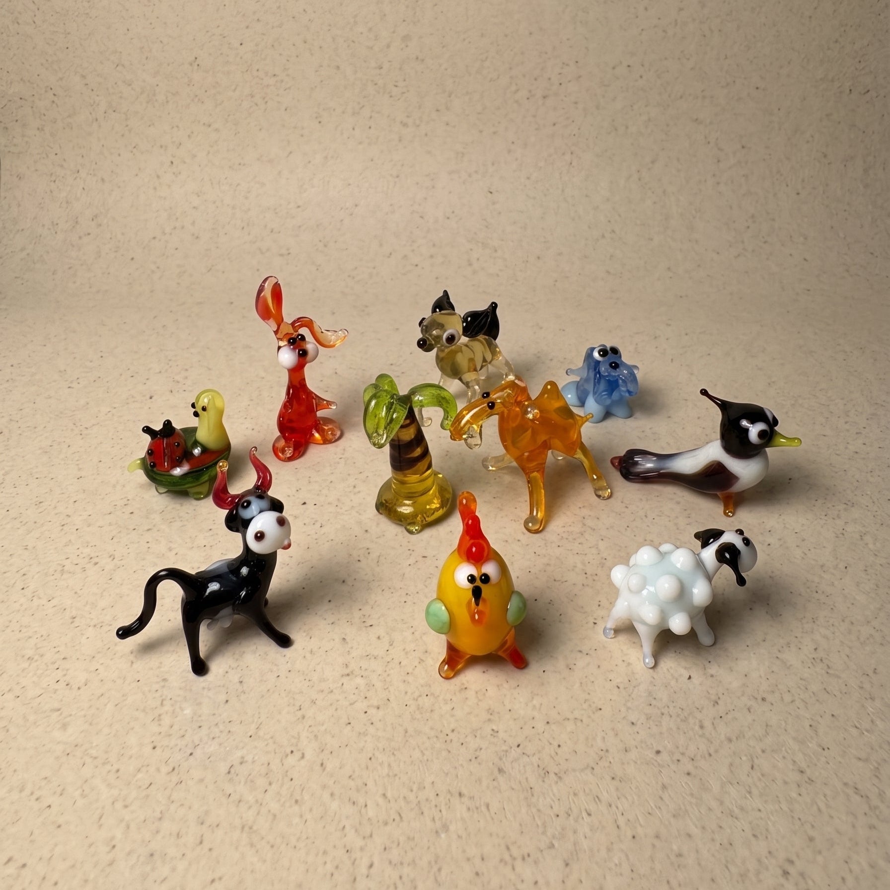 The Farmyard set of 10 miniature lampworked glass figurines including cow, rooster, sheep, lobster, horse, frog, palm tree, penguin, cat, and turtle, handcrafted by Glass by Iness in L'viv Ukraine