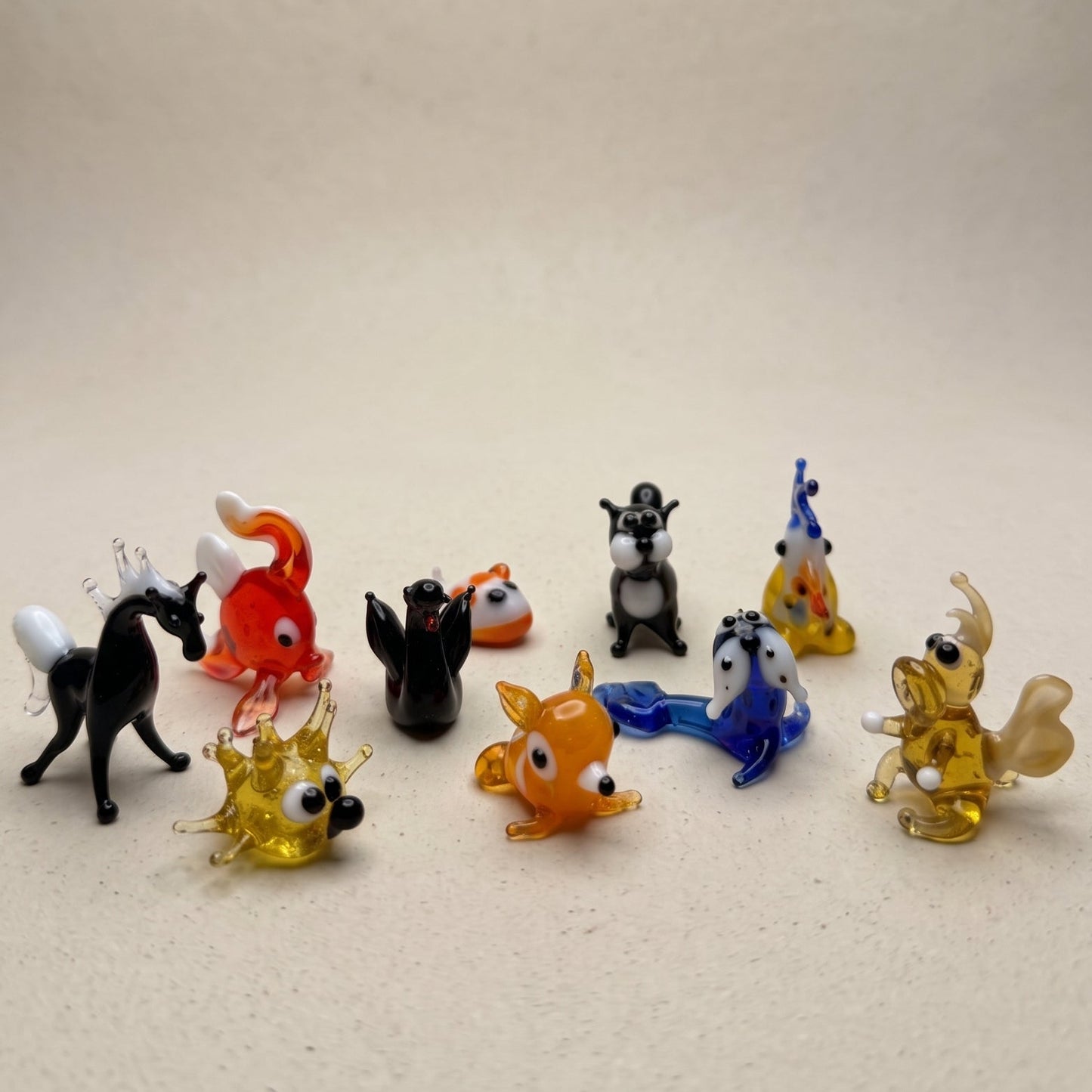 The Odd Bunch set of 10 miniature lampworked glass figurines including white rabbit, puppy, red lobster, teal frog, blue whale, yellow bee, white stork, and black cat, by Glass by Iness
