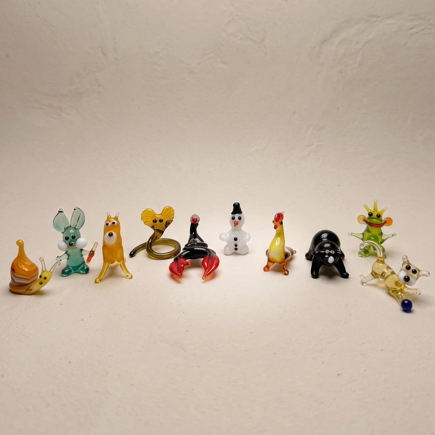 The Storybook set of 10 miniature lampworked glass figurines including orange snail, teal rabbit, yellow cat, cobra, snowman-dog, rooster, mole, frog prince, and golden cat, by Glass by Iness