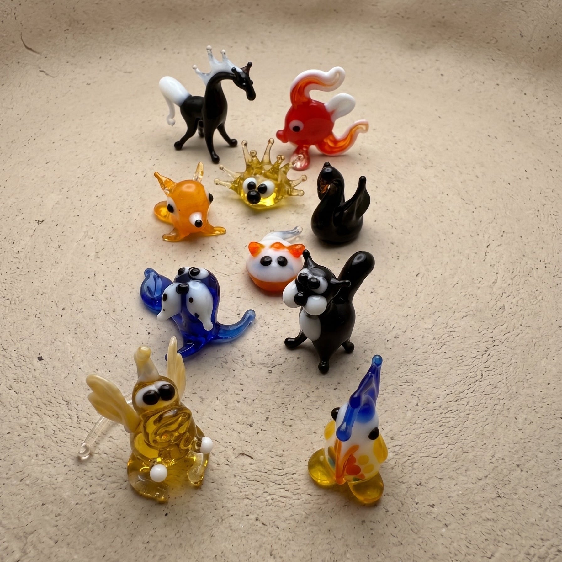 The Wild Ones set of 10 miniature lampworked glass figurines including black horse, red goldfish, orange fox, panda, blue dog, golden snail, black swan, and squirrel, by Glass by Iness