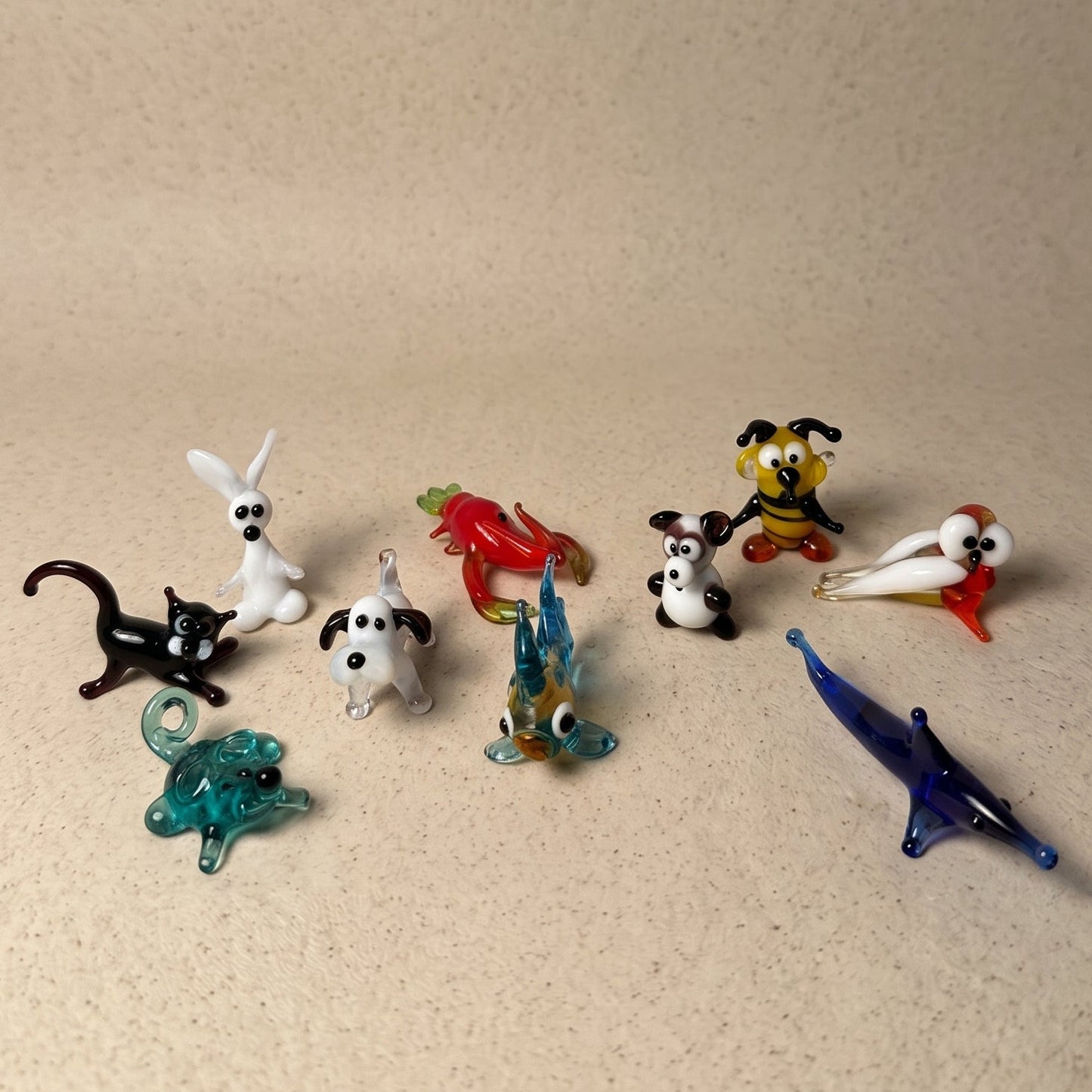 Three miniature lampworked glass figurines — bull with red horns, penguin, and spotted dog — showing individual face character, by Glass by Iness