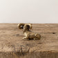 Reclining brass ram figurine with curled horns and antique patina, displayed on a rustic wooden surface
