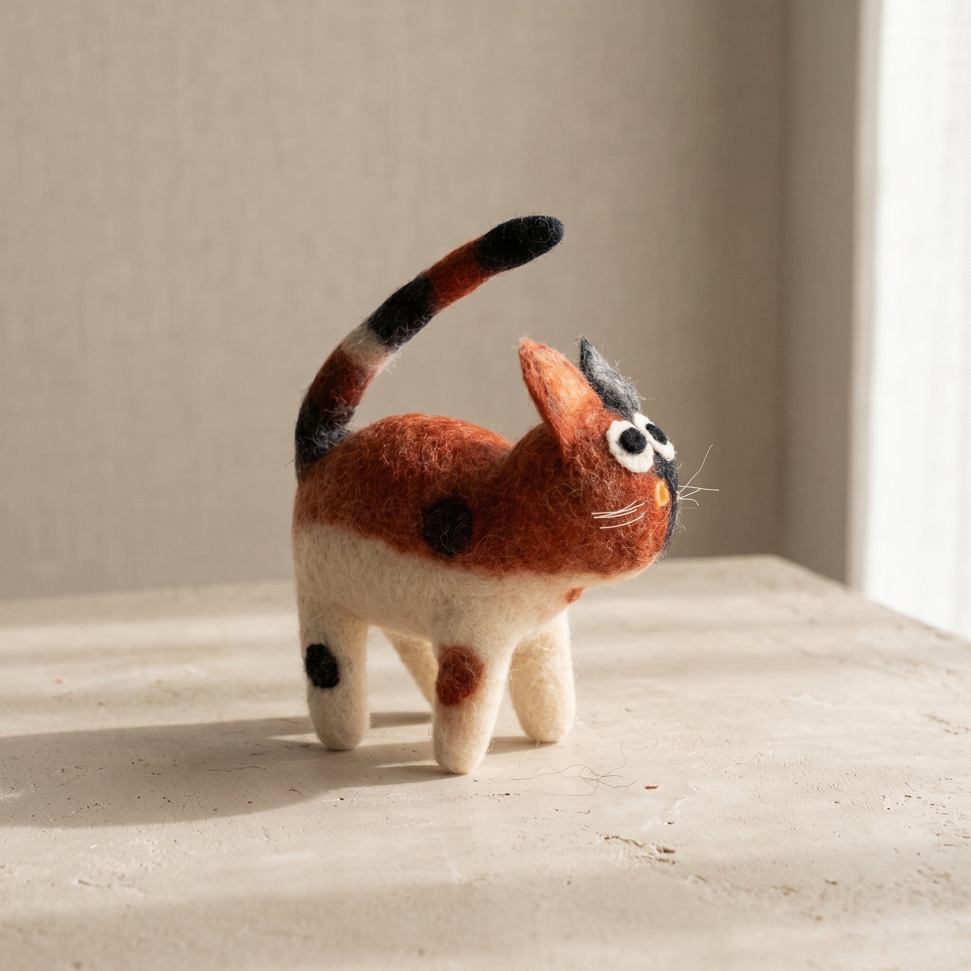 Side view of the calico felt cat showing its striped tail held upright and spotted markings