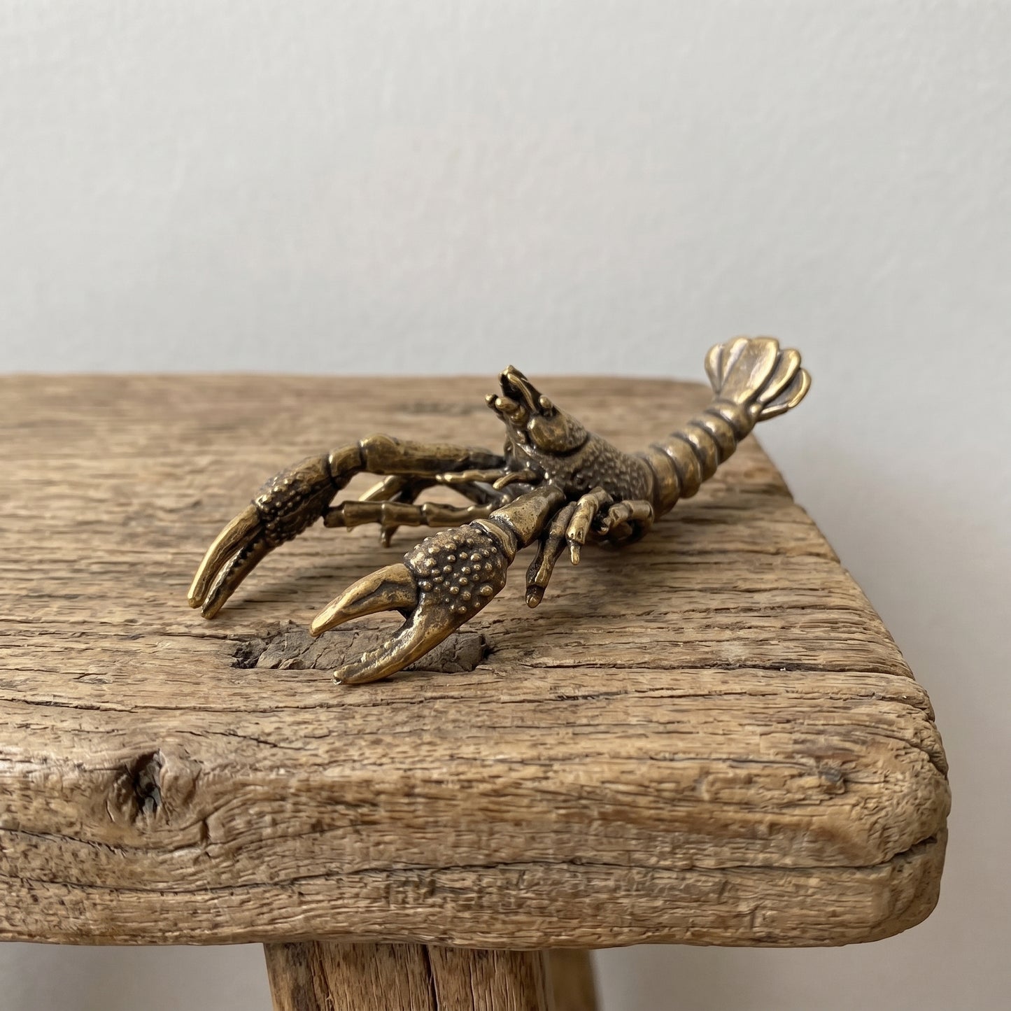 Front view of a brass crawfish figurine showing its two large pincers and detailed walking legs with antique patina