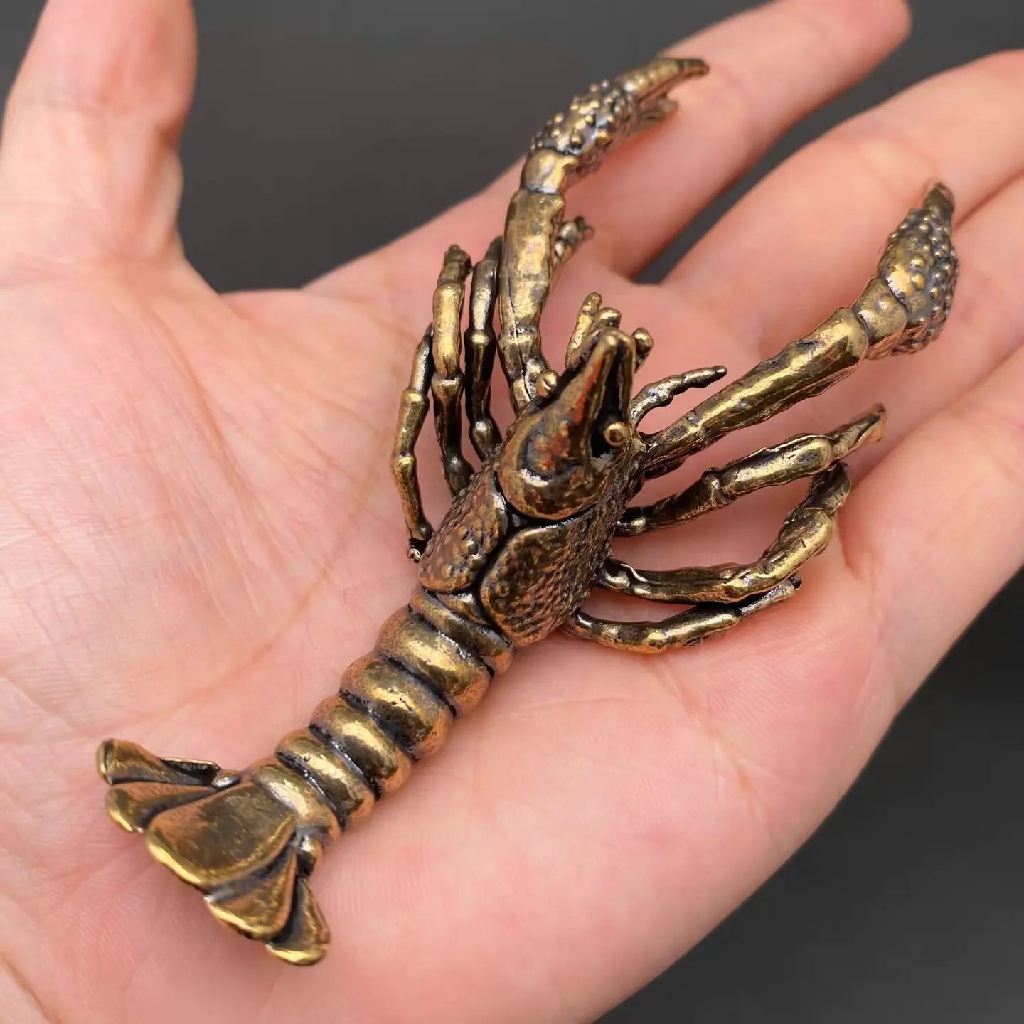 Brass crawfish figurine held in an open hand to show its palm-sized scale and heft