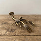Solid brass crawfish figurine with raised claws and curled tail, antique patina finish, displayed on a clear stand