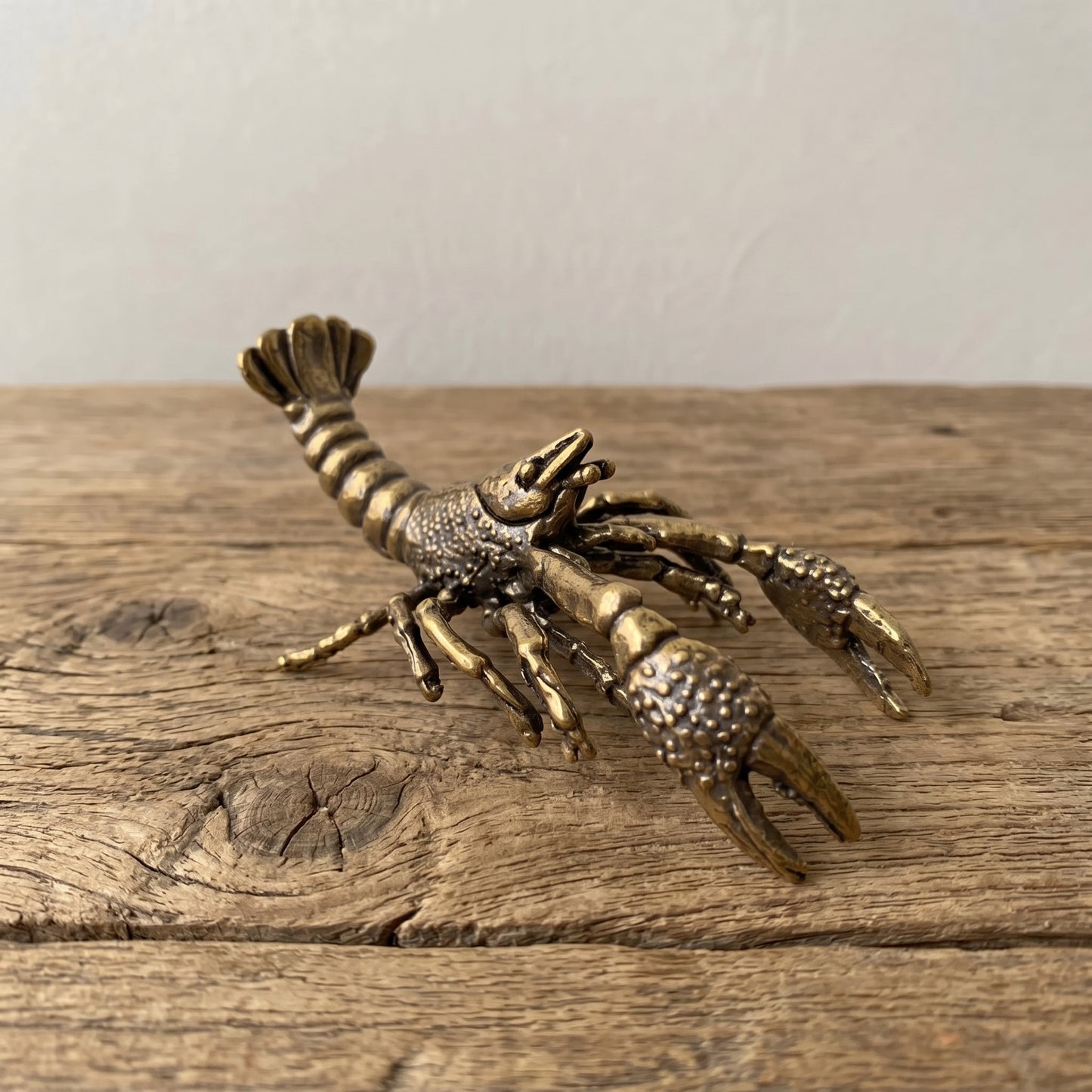 Solid brass crawfish figurine with raised claws and curled tail, antique patina finish, displayed on a clear stand