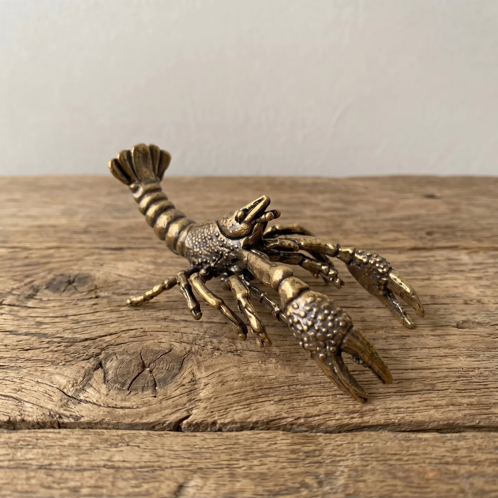 Solid brass crawfish figurine with raised claws and curled tail, antique patina finish, displayed on a clear stand