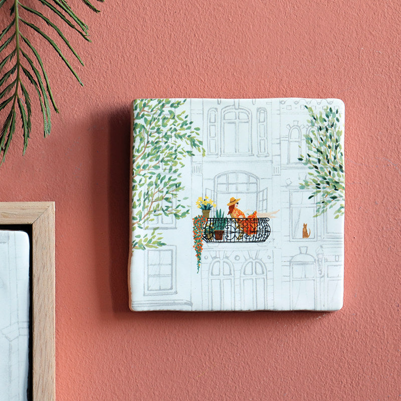 My Favorite Spot Storytile displayed on a warm-toned wall showing illustration of a person with cats on a sunny balcony, hand-baked ceramic by Marga van Oers in the Netherlands, from WILLAGE