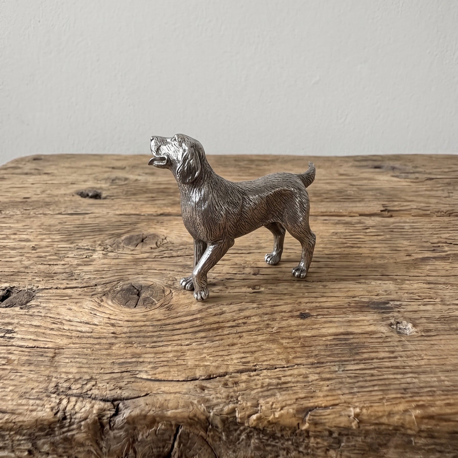 Pewter retriever figurine with raised tail and detailed coat, displayed on a rustic wooden surface