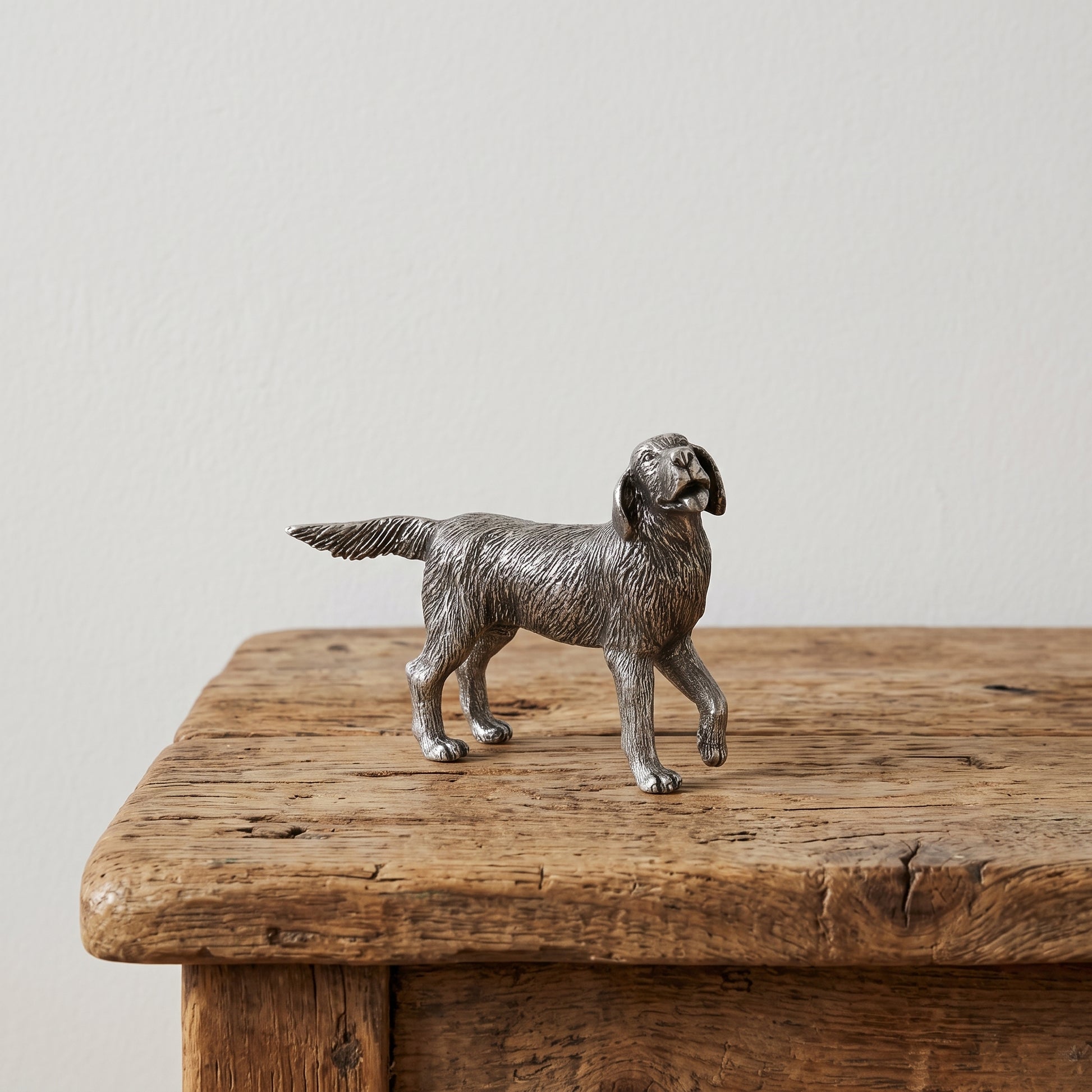 Side view of a pewter retriever figurine with lifelike coat detail, standing on a weathered wood table