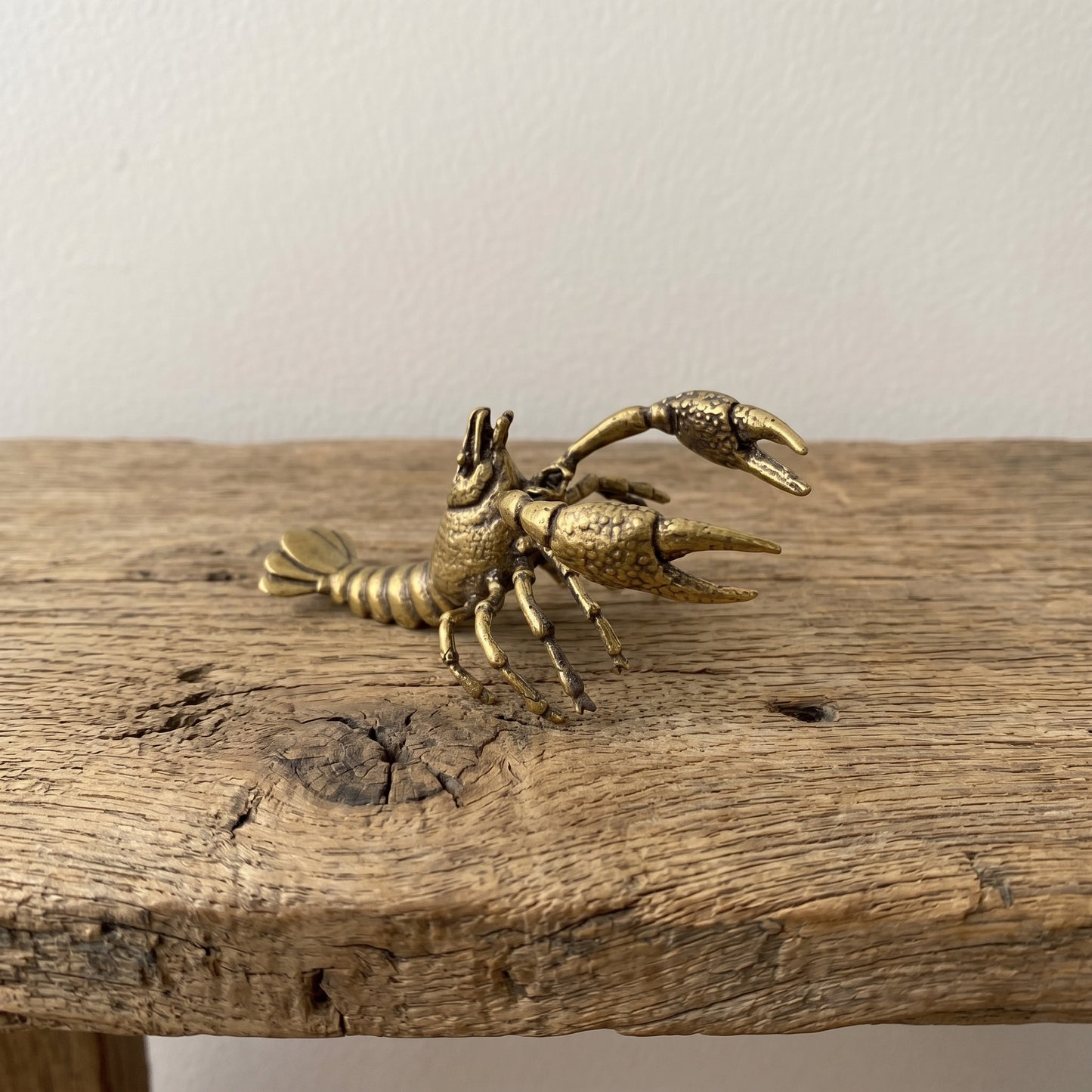 Side view of a brass lobster figurine showing the segmented tail, walking legs, and detailed claws with antique patina
