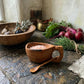 Reclaimed olive wood salt pot filled with pink salt alongside fresh herbs and vegetables in kitchen setting