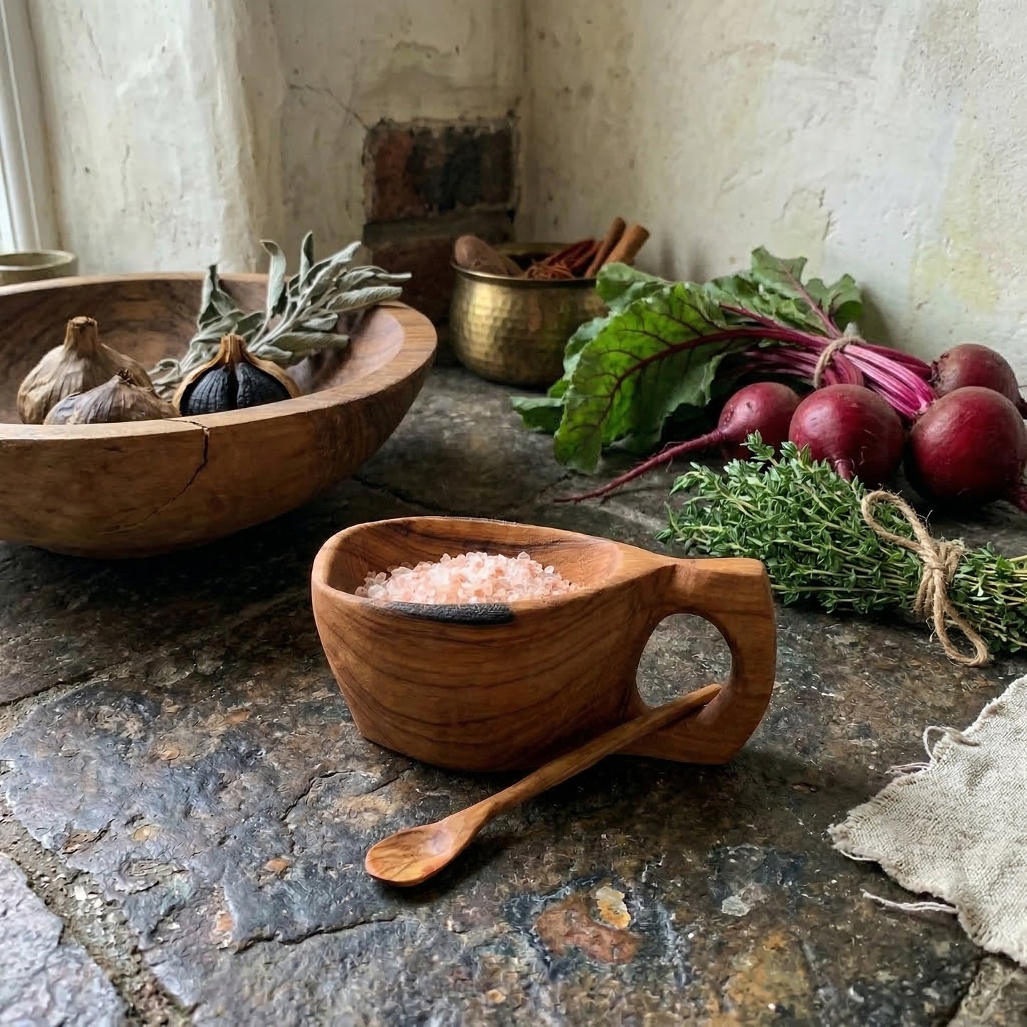 Reclaimed olive wood salt pot filled with pink salt alongside fresh herbs and vegetables in kitchen setting