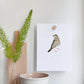  Magnetic beech wood wall holder gripping a bird art print on a white wall, held in place between two wooden blocks
