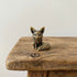 The Playful Kit miniature brass baby fox sitting upright on a wooden surface, with perked ears and warm aged patina, from the WILLAGE Tiny Objects collection