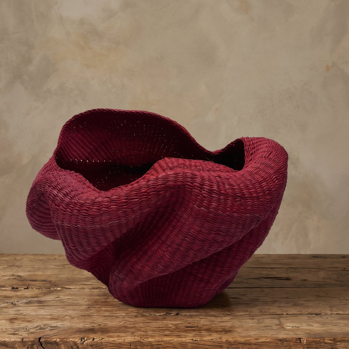 Red handwoven Bolga sculpture basket with a wide, folded opening and twisting elephant-grass form, by Nanasei Agyemang, Ghana
