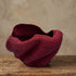 Red handwoven Bolga sculpture basket with a wide, folded opening and twisting elephant-grass form, by Nanasei Agyemang, Ghana