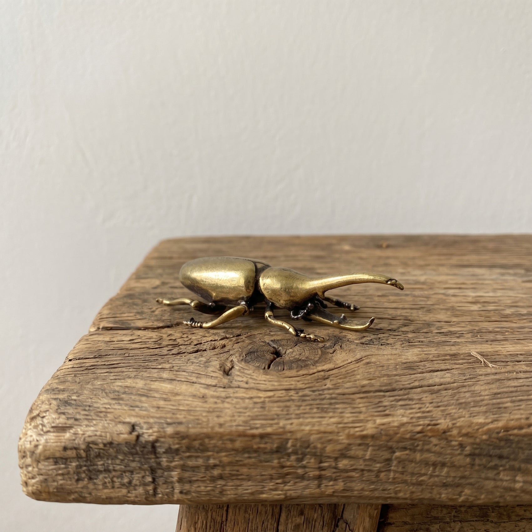 The Powerhouse miniature solid brass rhinoceros beetle figurine with a curved horn, held in a hand to show scale