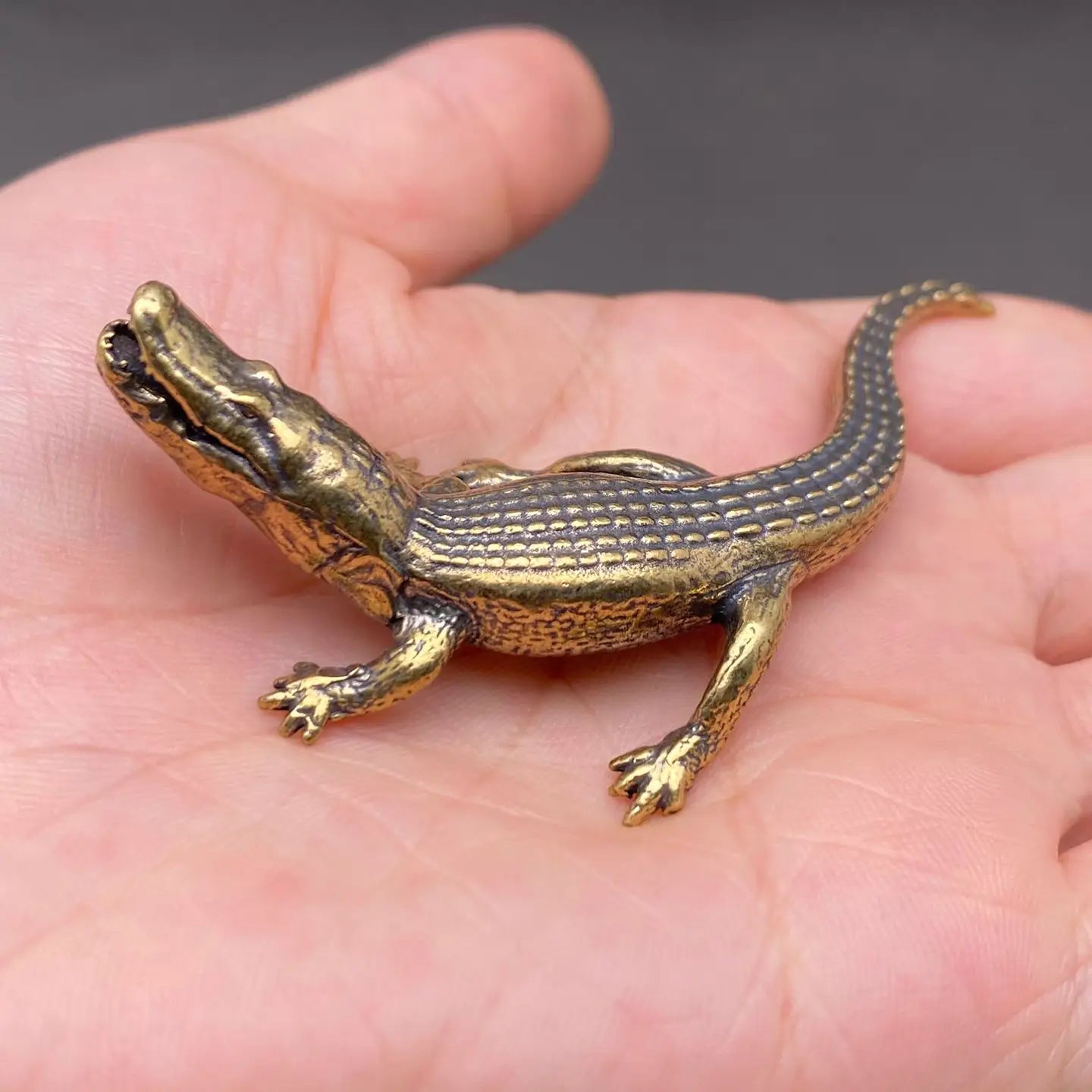 The Primal Sentinel miniature brass crocodile held in hand to show scale, with open jaws and golden patina
