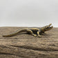 The Primal Sentinel miniature brass crocodile lying flat on a wooden surface, showing detailed scutes and warm aged patina, from the WILLAGE Tiny Objects collection