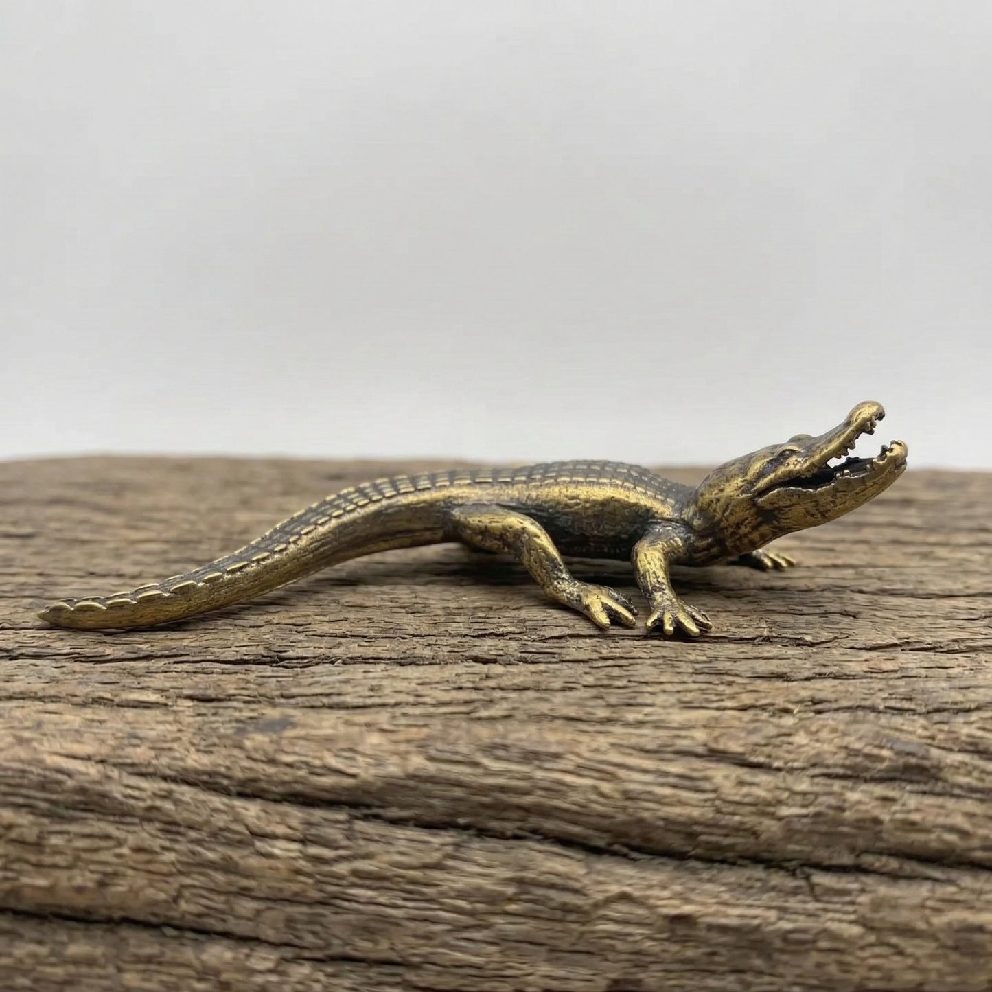 The Primal Sentinel miniature brass crocodile lying flat on a wooden surface, showing detailed scutes and warm aged patina, from the WILLAGE Tiny Objects collection