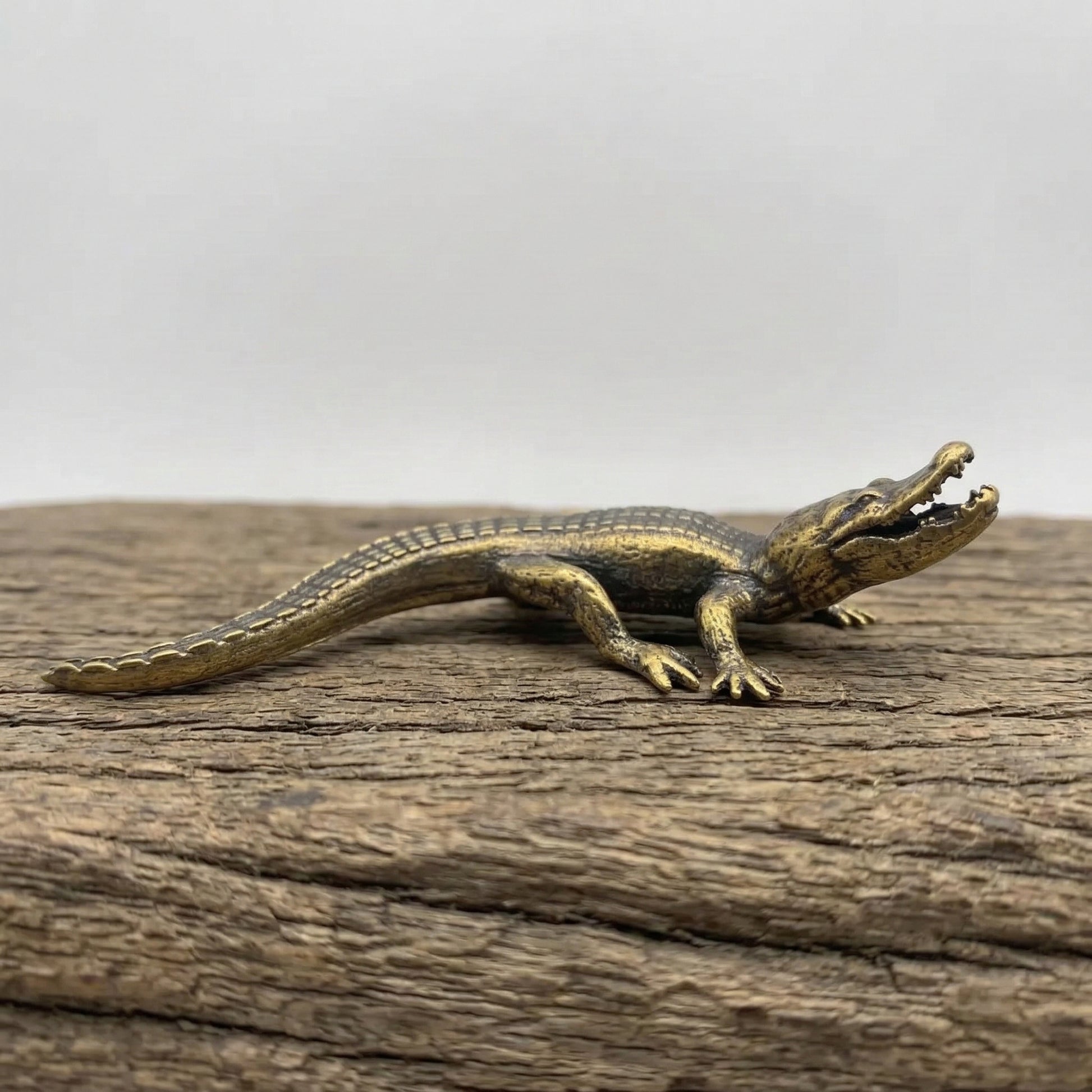 The Primal Sentinel miniature brass crocodile lying flat on a wooden surface, showing detailed scutes and warm aged patina, from the WILLAGE Tiny Objects collection