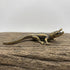 The Primal Sentinel miniature brass crocodile lying flat on a wooden surface, showing detailed scutes and warm aged patina, from the WILLAGE Tiny Objects collection