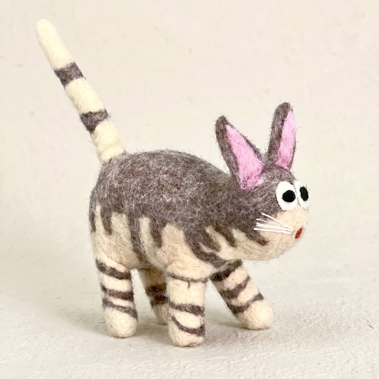 Front three-quarter view of a hand-felted grey tabby cat showing its wide eyes, whiskers and stitched red nose